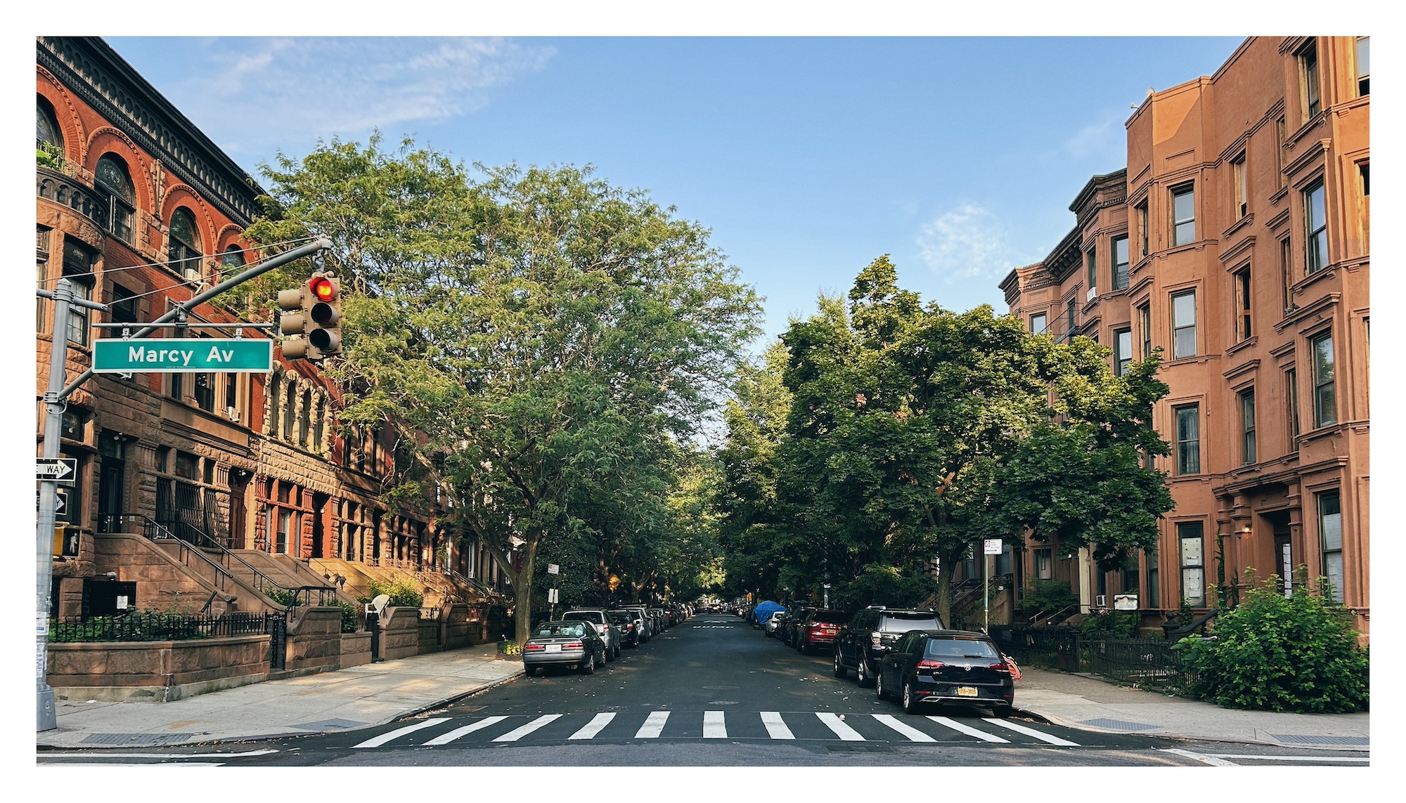 a view down a tree-lined street in the early morning; on either side of the street, the red brick buildings glow in the morning light; a bright blue sky overhead