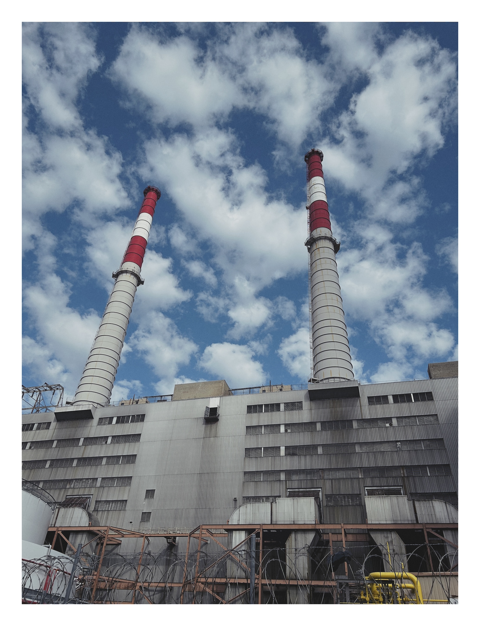 two tall smokestacks, striped with red and white, loom above a power generating station