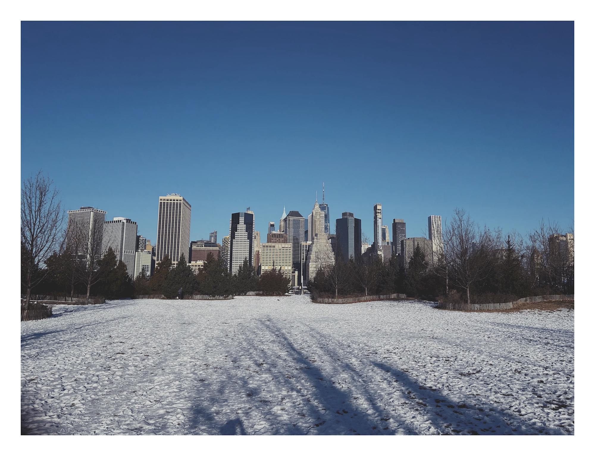 the skyline of lower Manhattan as seen from a snow-covered pier in Brooklyn Bridge Park