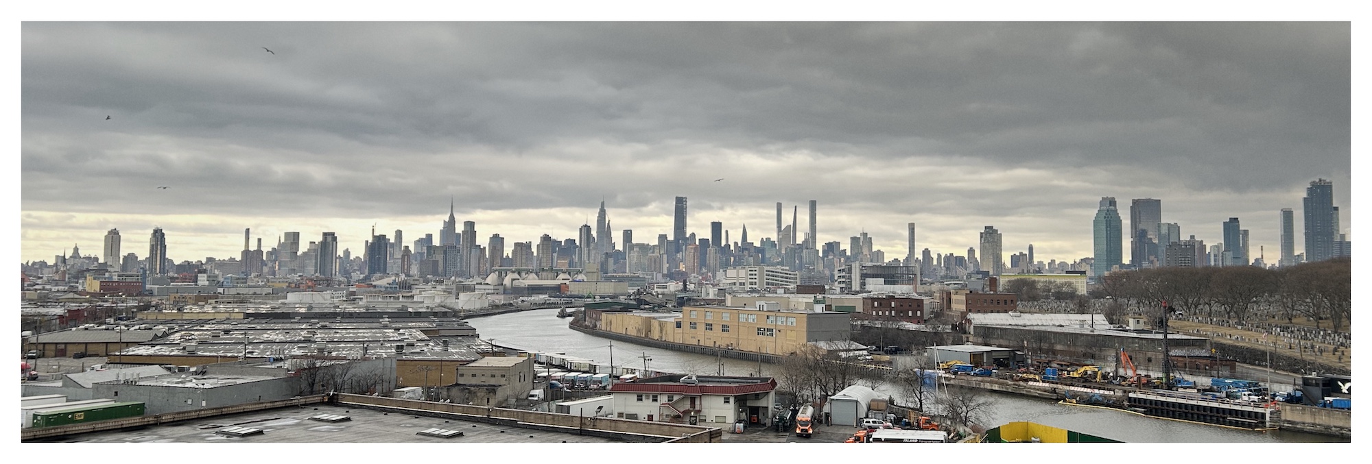 skyline of Manhattan, as seen from the Kosciuszko Bridge, silhouetted against a cloud-covered sky