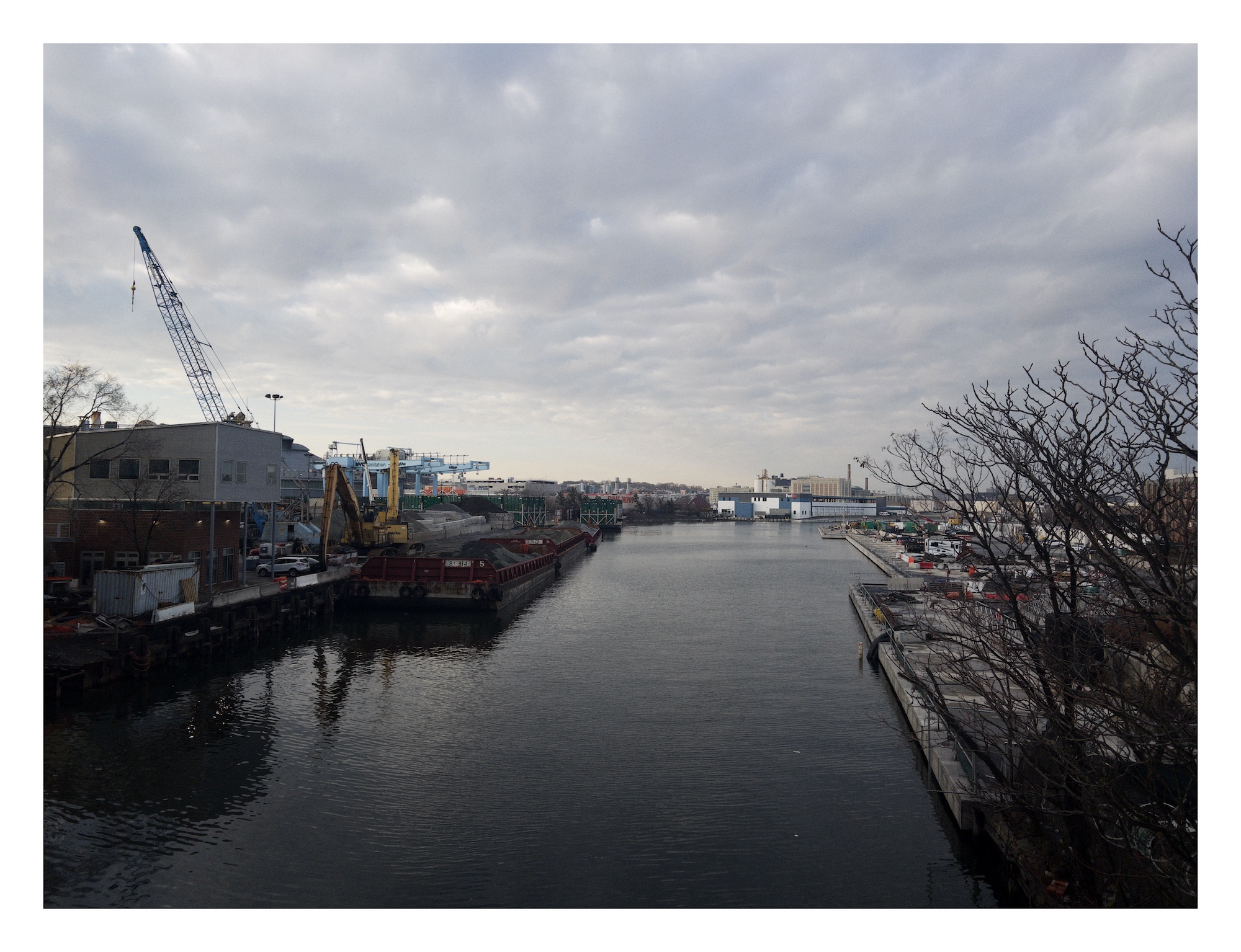 a straight-edged canal courses between industrial docks and warehouses under a cloudful sky