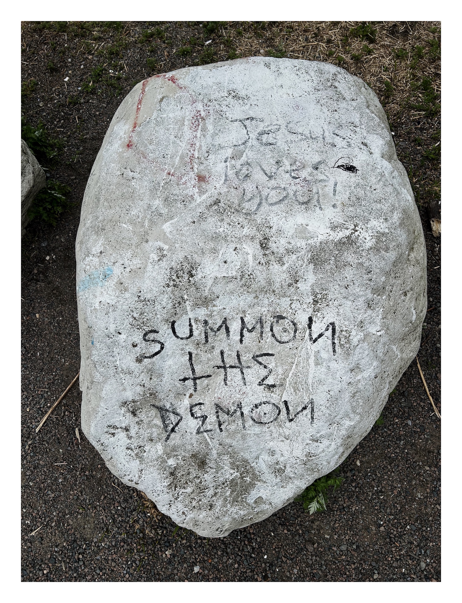 a pale boulder with two prominent graffiti writings: "Jesus loves you!" and "summon the demon"