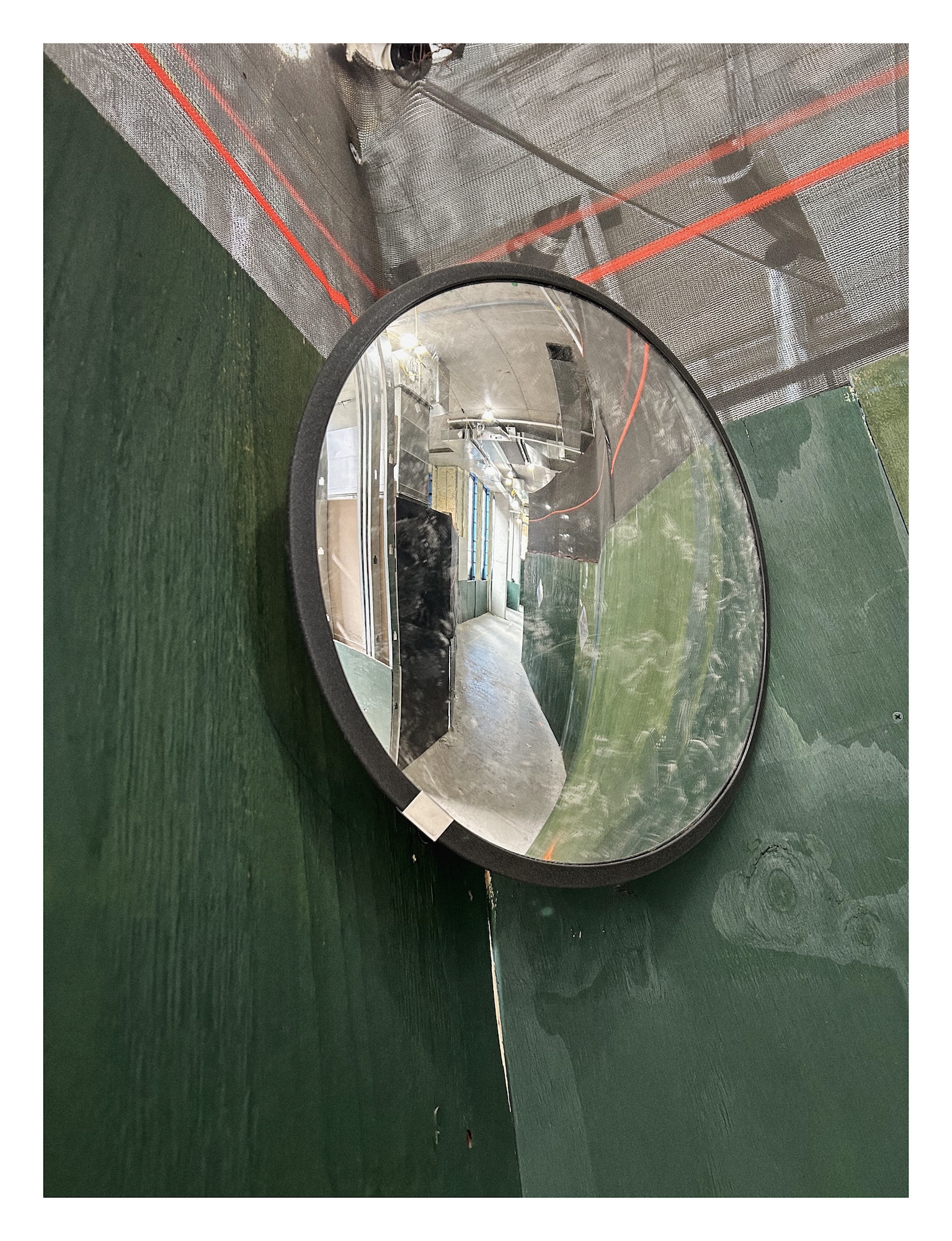 a convex mirror is mounted in the corner between two green walls, and reflects a winding path between them