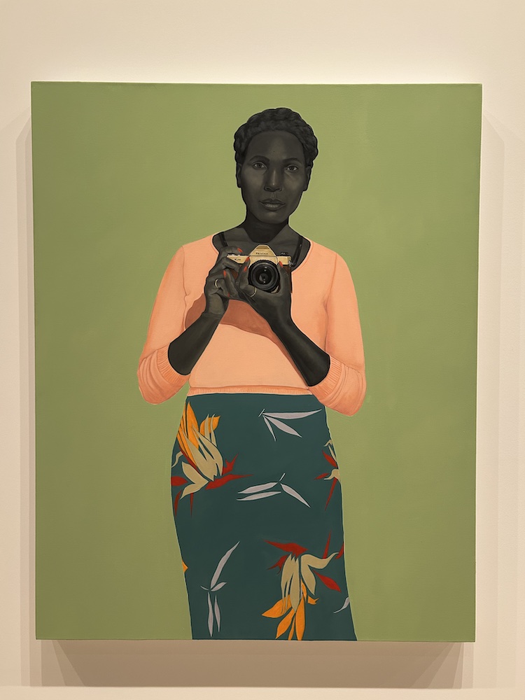 painting by Amy Sherald of a woman with a peach sweater and teal skirt points a camera and her gaze the viewer; the background behind her is a solid soft natural green