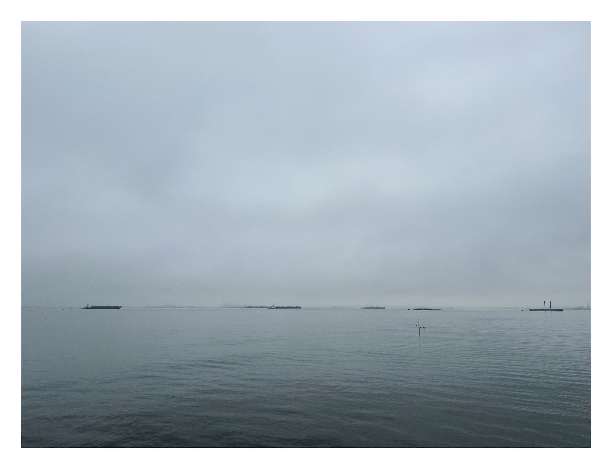 long distant cargo ships skim the edge between a grey sky and  a grey sea
