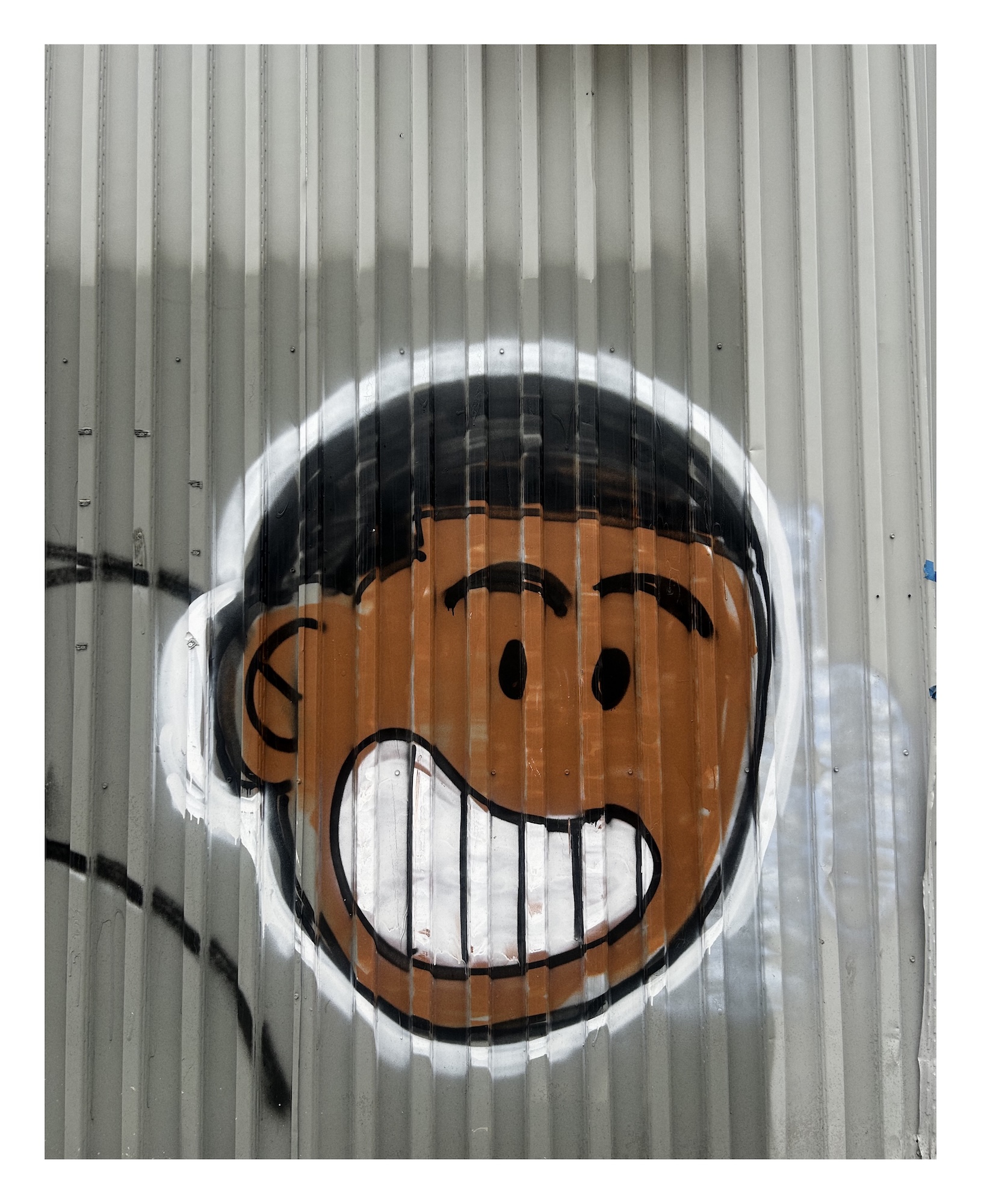 a cartoonish image of a black youth with a big gleaming spile is spray-painted on ridge metal siding