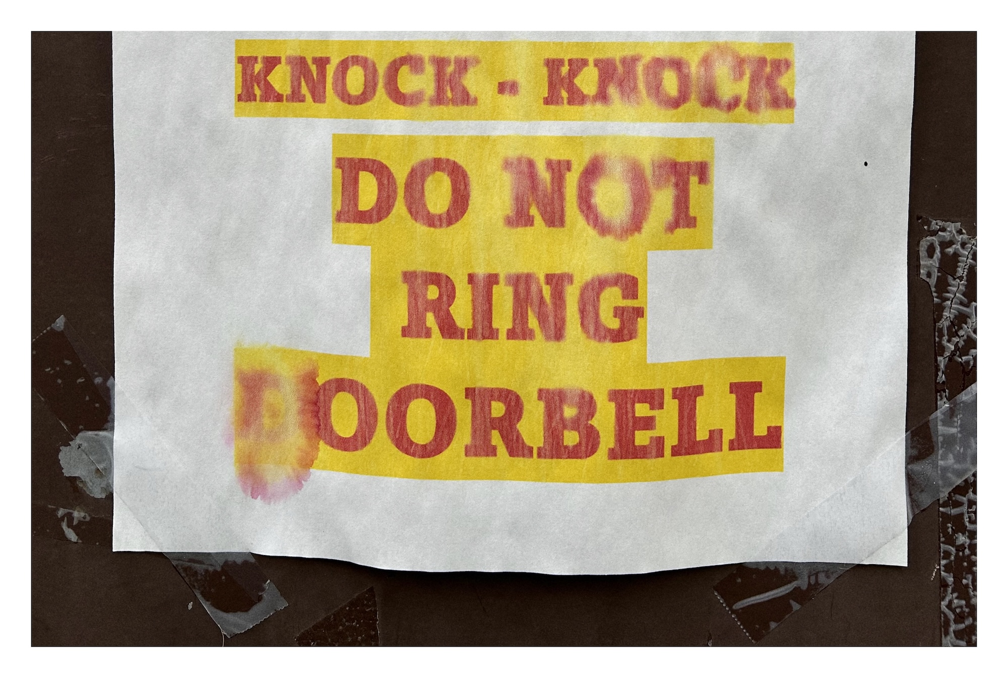 paper sign on a church door with the words 'KNOCK-KNOCK DO NOT RING DOORBELL' printing in red text highlighted in yellow