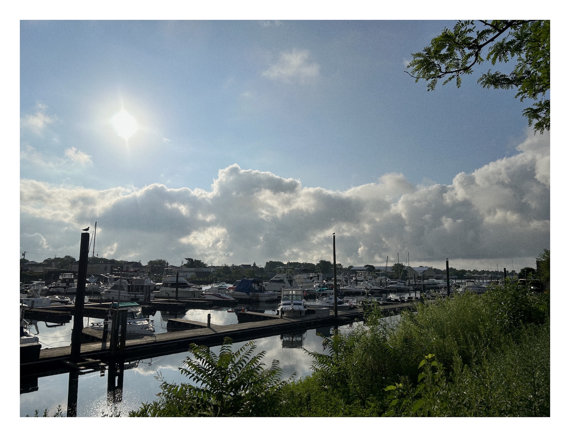 view of boats tied to wooden docks, with fluffy clouds and bright sun in the background