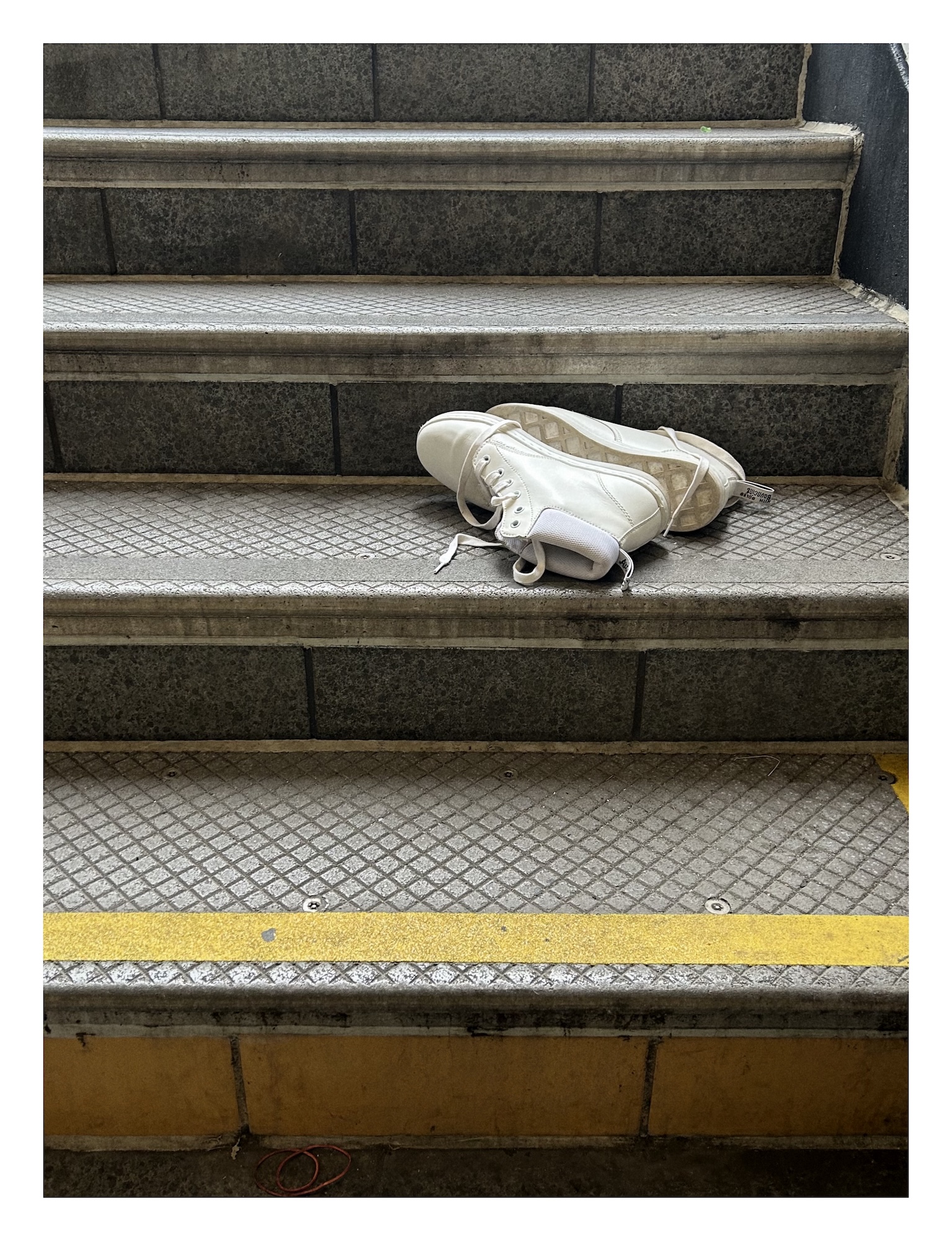clean white high-top shoes lie on their side on the grey gritty steps up from a subway platform