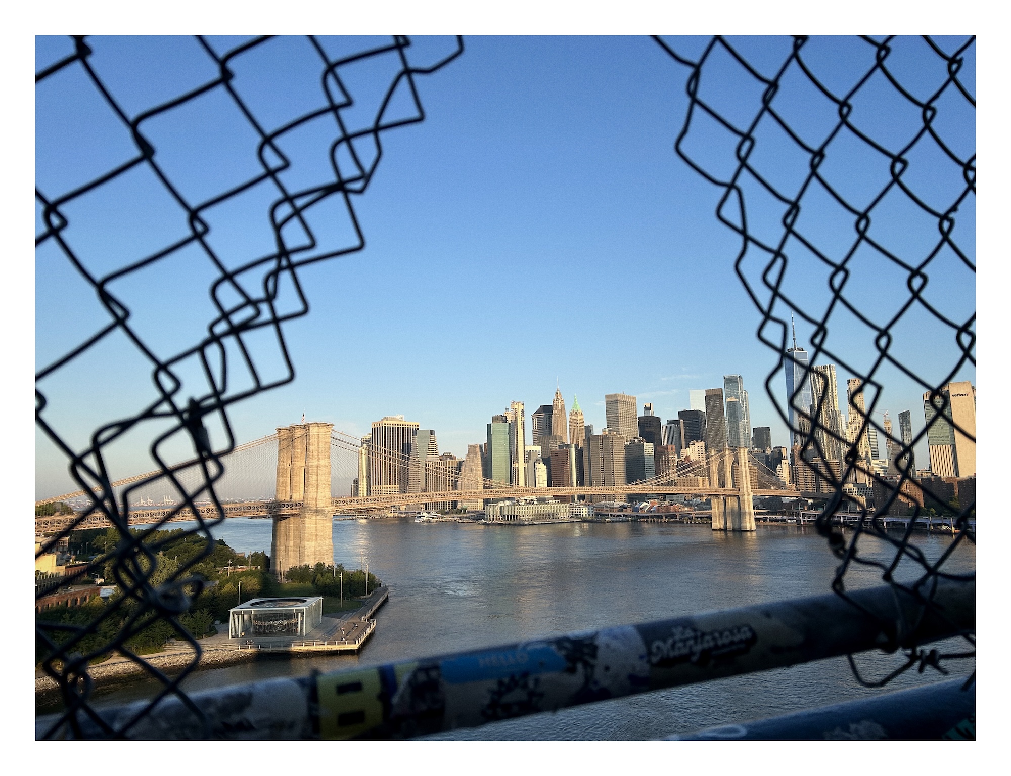 view of the Brooklyn Bridge through a gap in a chain link fence