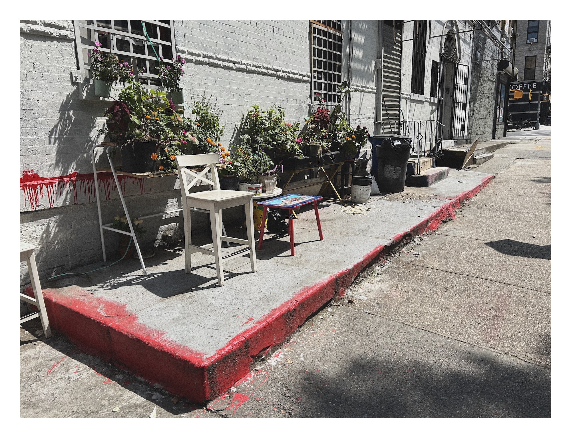 a stool and footrest on a sunny sloping sidewalk with potted plants
