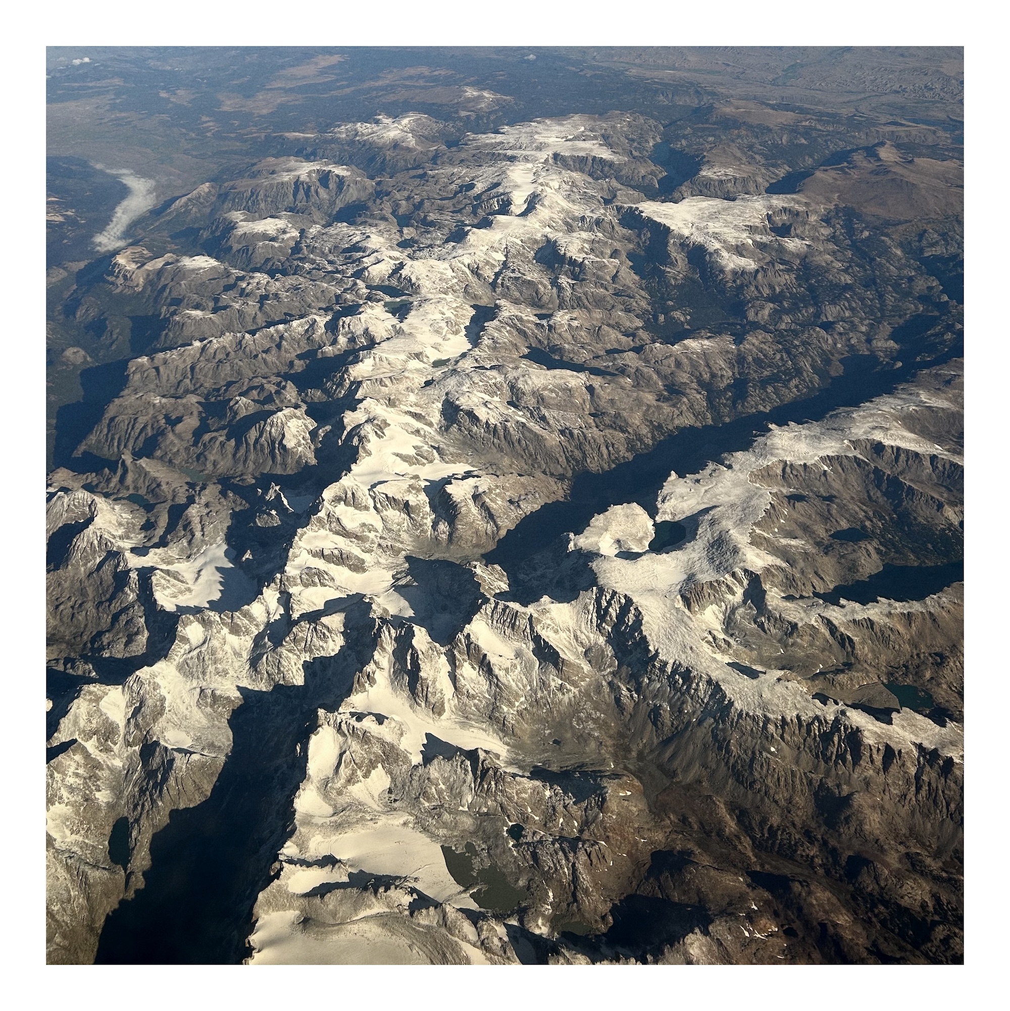 white snow covers dark mountains seen from high above; view of the Wind River Range of the Rocket Mountains as seen from airplane height