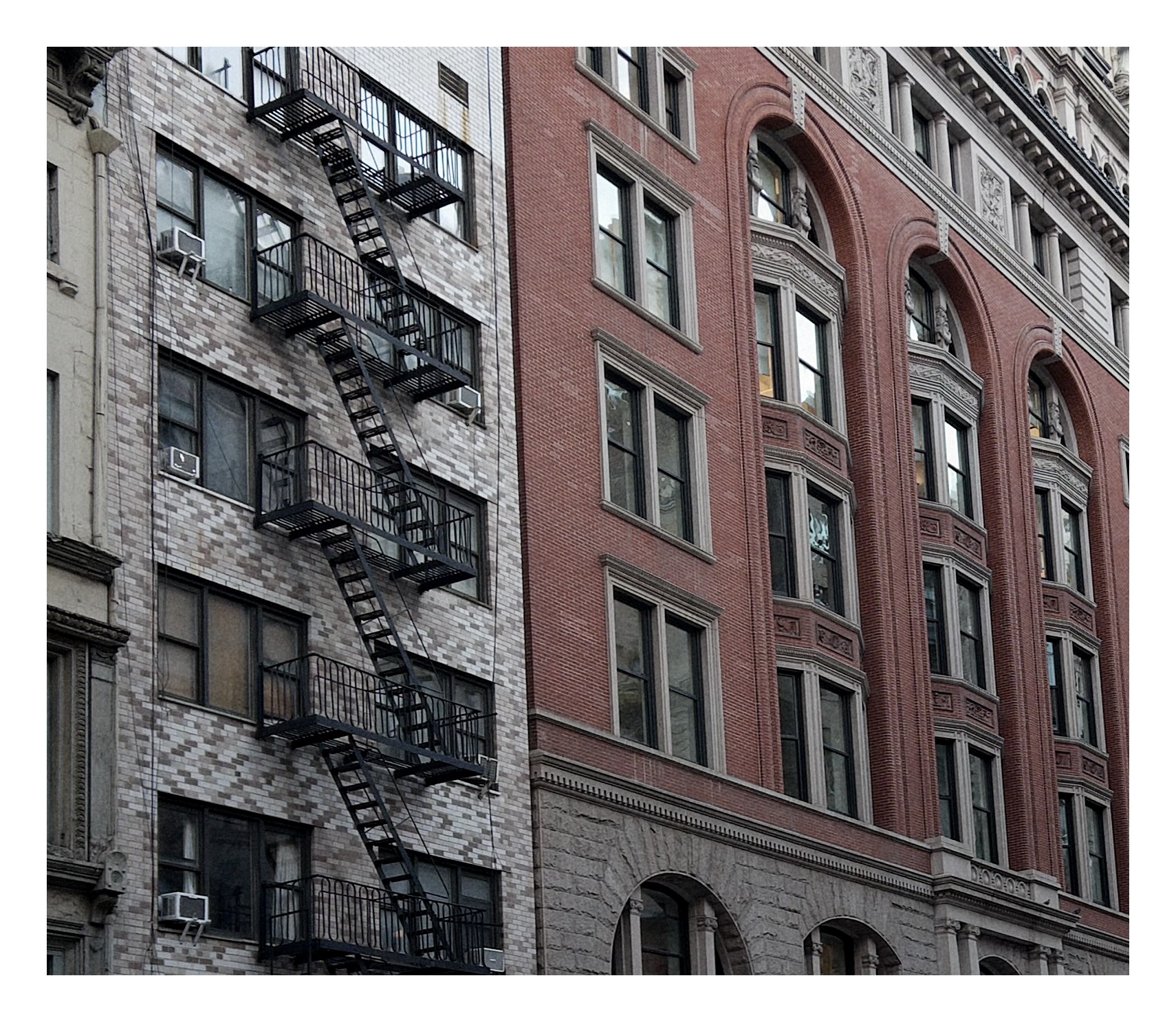 a wall of manhattan buildings fills the frame with a grid of windows, one building made of pale grey and beige bricks the other red