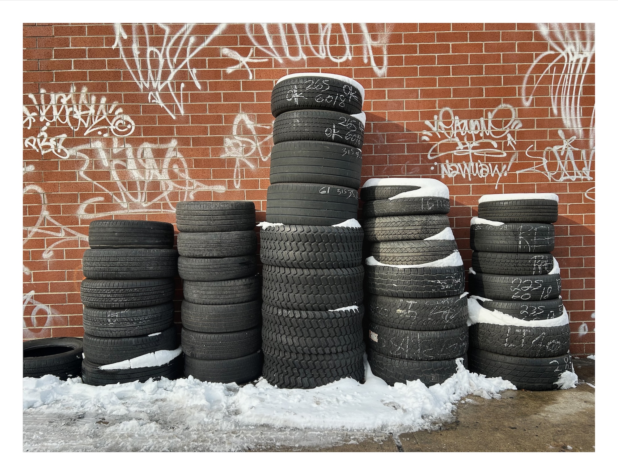 stacks of tires next to a brick wall, with snow piled on top and around them