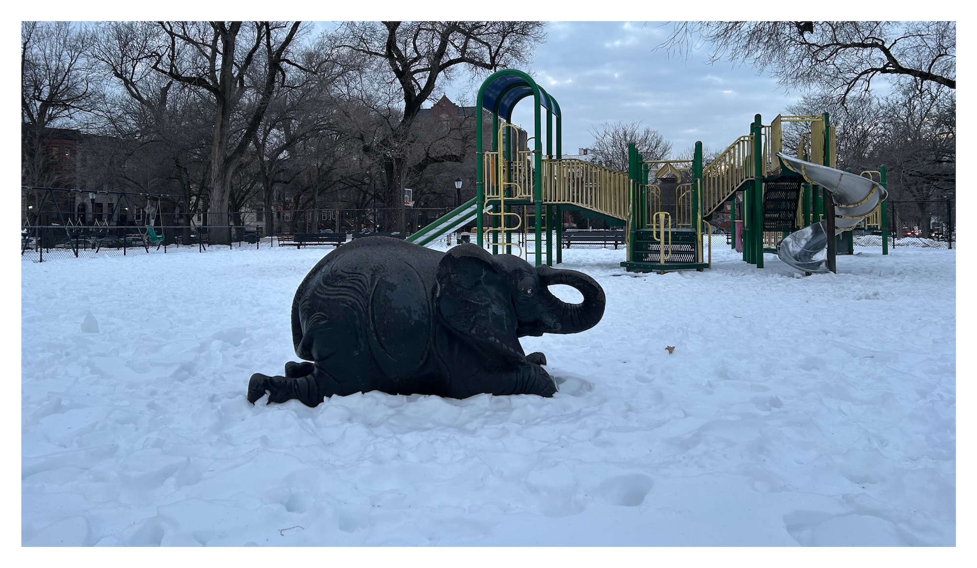bronze statue of an elephant reclining, placed in a snow-covered playground