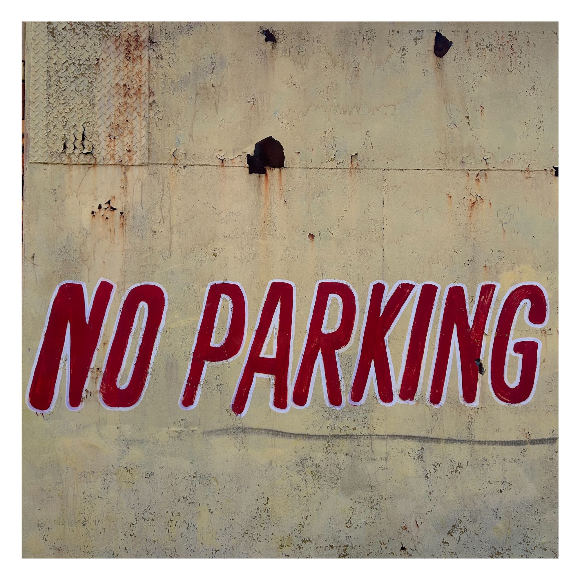 hand-painted sign on a concrete wall reading 'No Parking' in large red capital letters with white borders