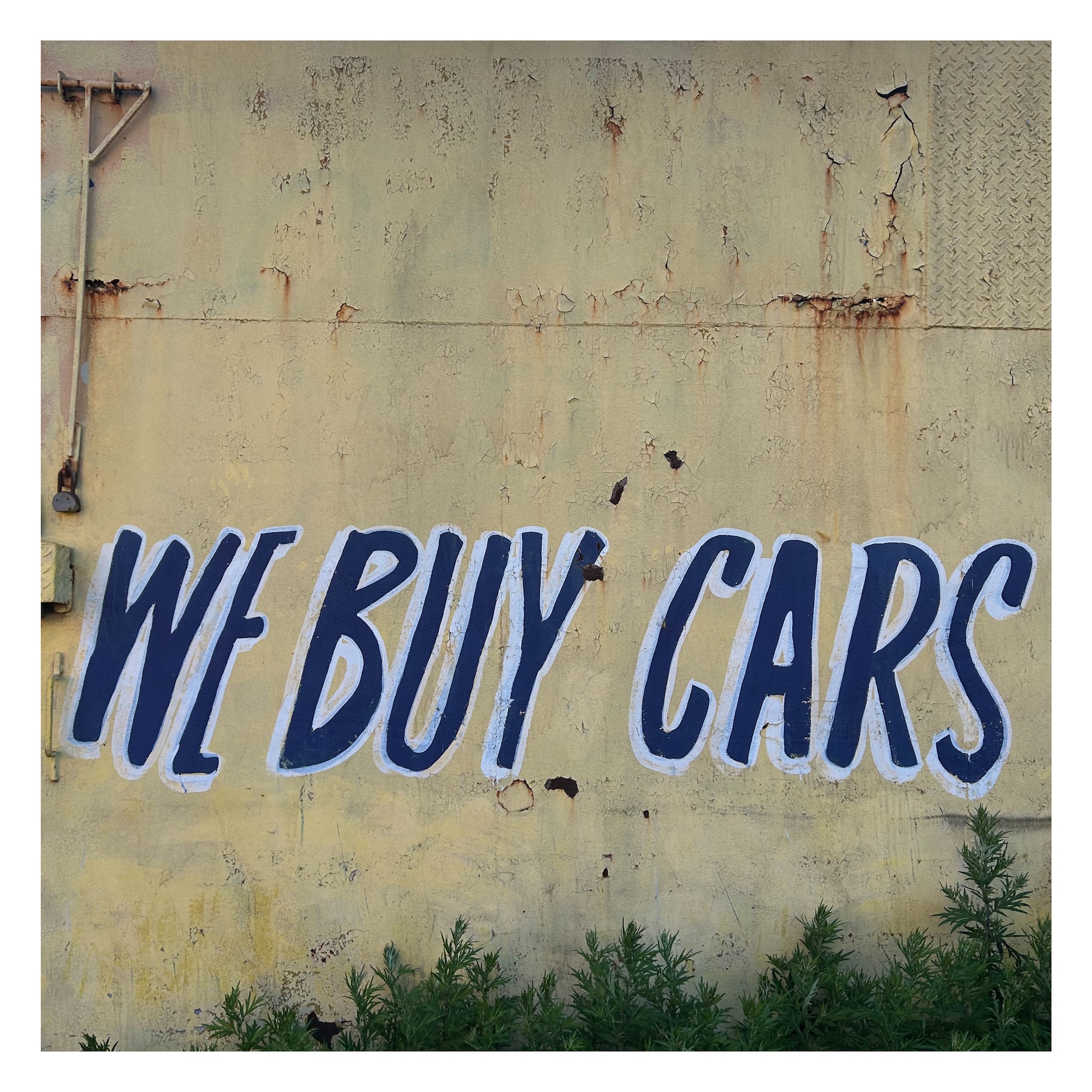 hand-painted sign on a concrete wall reading 'We Buy Cars' in large blue capital letters with white borders