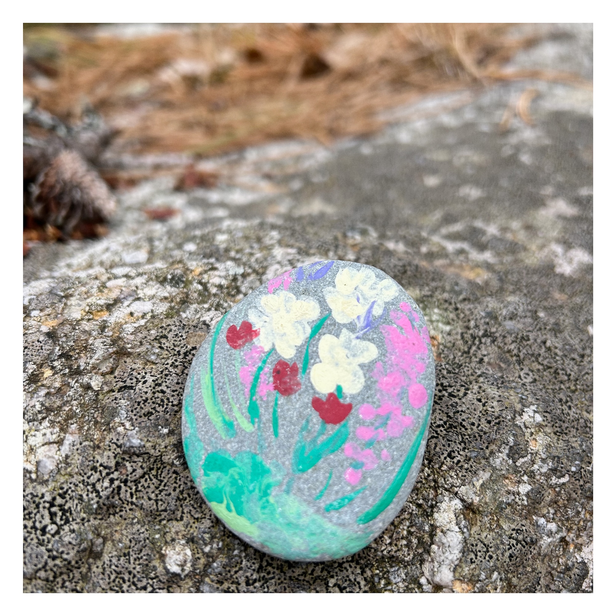 small round stone with a painting of flowers rests on a large boulder