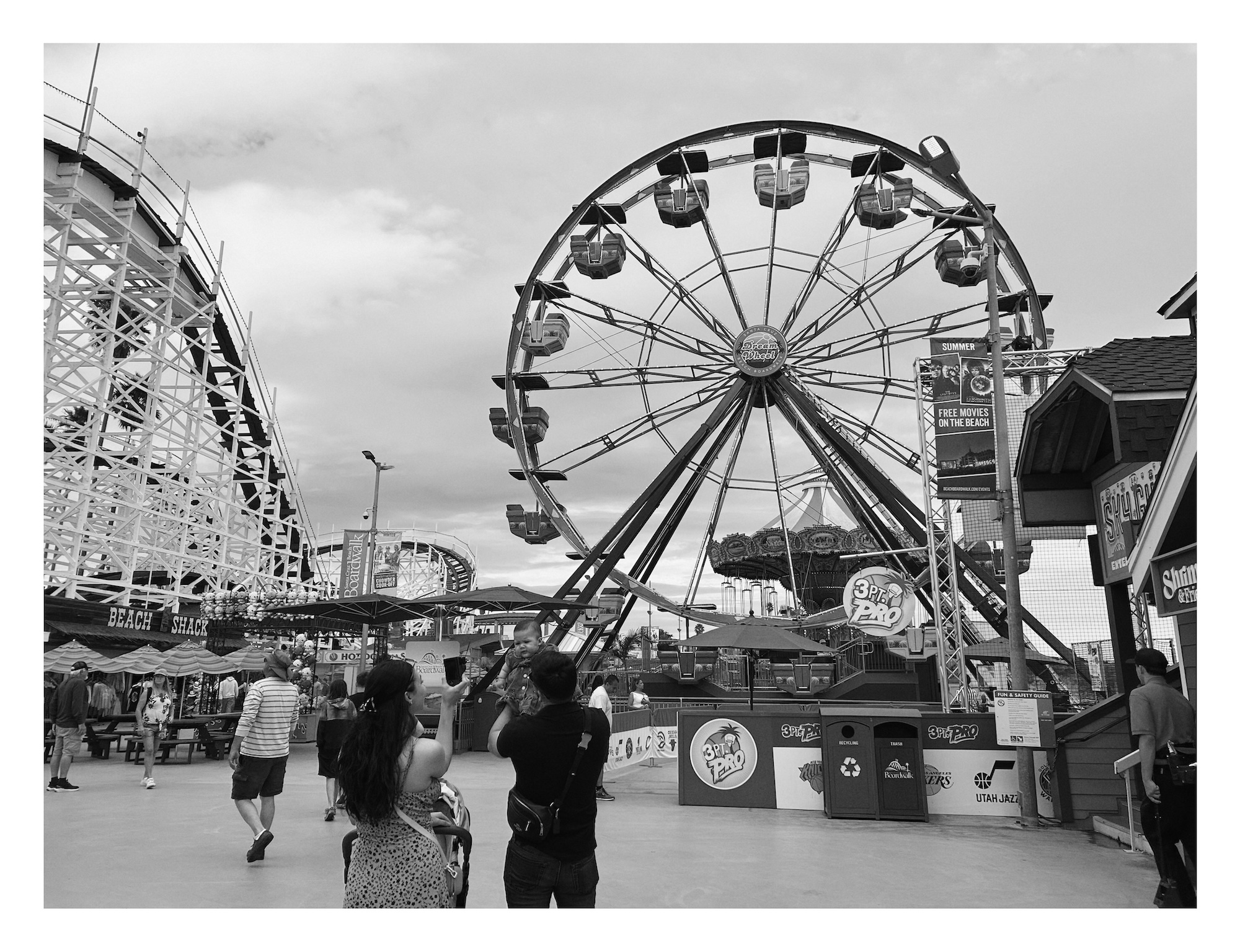 a couple takes a photo of their baby in front of the ferris wheel on the Santa Cruz boardwalk