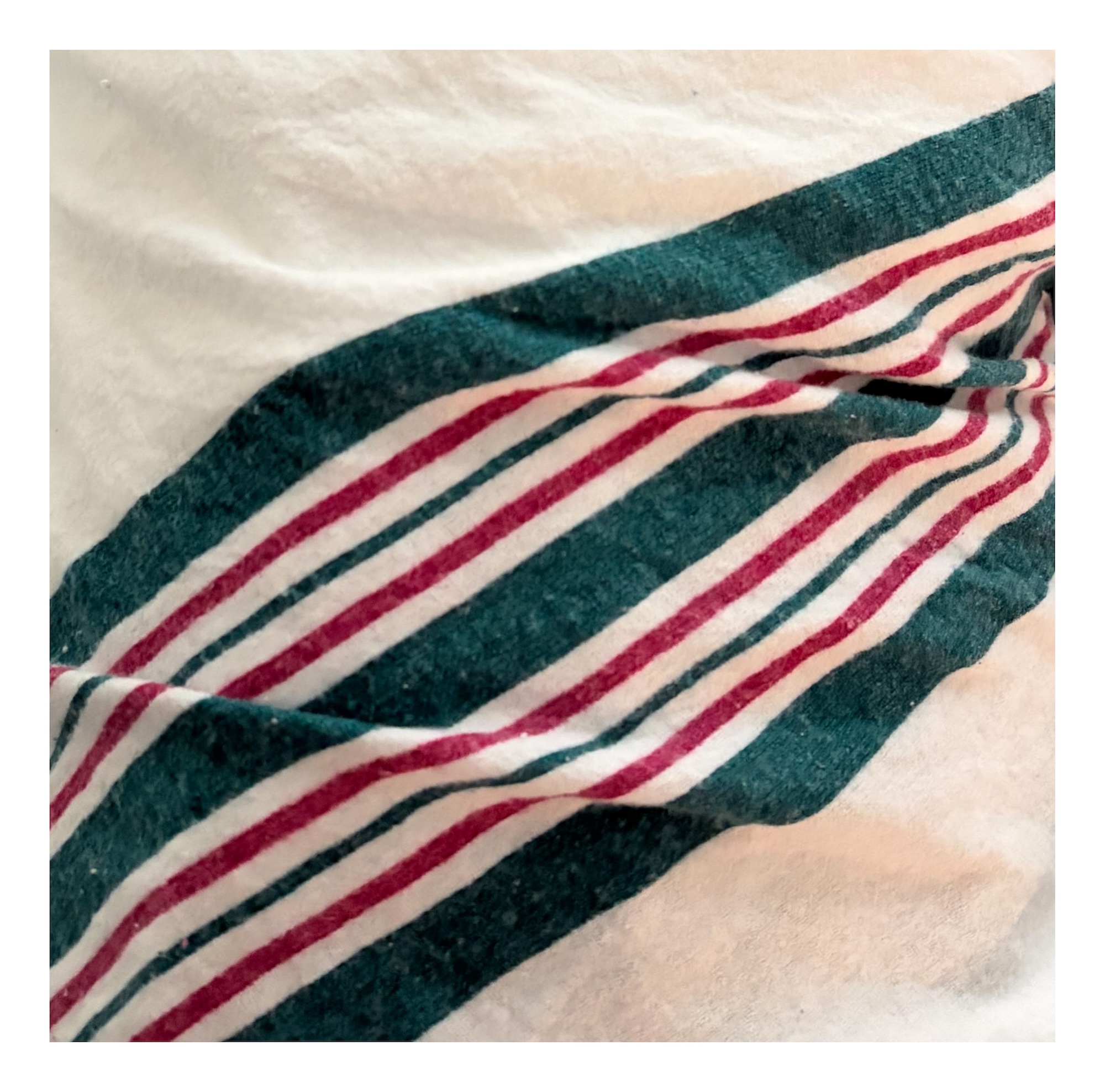 close-up of a baby's swaddle, with teal and maroon stripes tracing an angle across the rippled white fabric