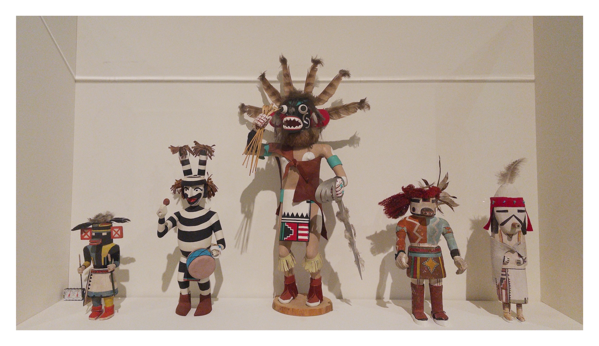 a row of five colorful kachina dolls in a display case in the Brooklyn Museum